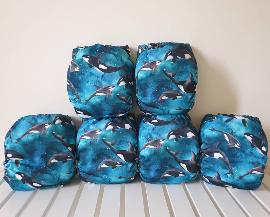 6 nappies stacked in two rows with a print showing orcas swimming in a blue galaxy